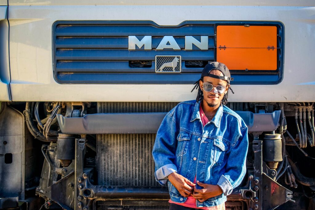A man walking smiling with the hood of his MAN semi-truck in the background