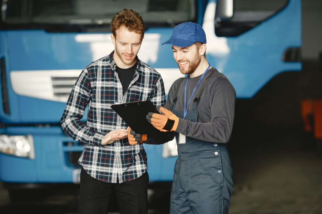 Smiling truck mechanic pointing to a clipboard with a customer looking at the clipboard and smiling