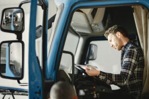 A person sitting in the driver's seat in a semi truck reviewing what appears to be a stack of papers on the driver's wheel