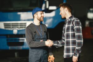 A mechanic and customer smiling and shaking hands in the foreground with a fleet vehicle in the background