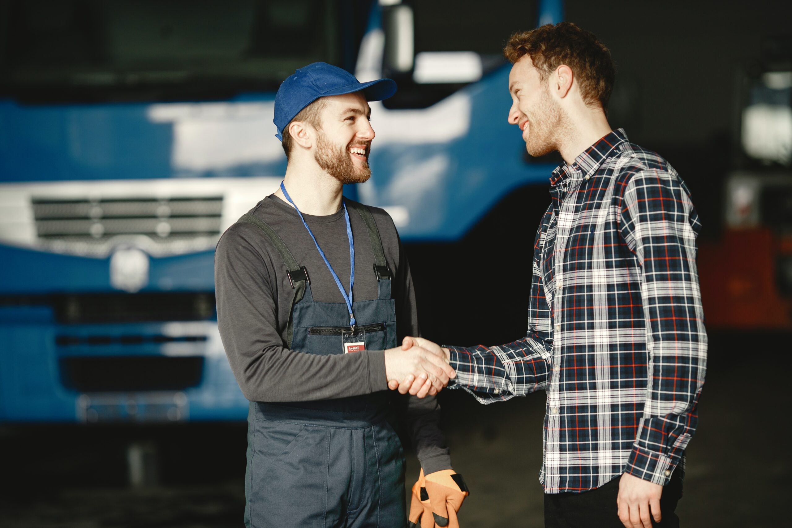 A mechanic and customer smiling and shaking hands in the foreground with a fleet vehicle in the background