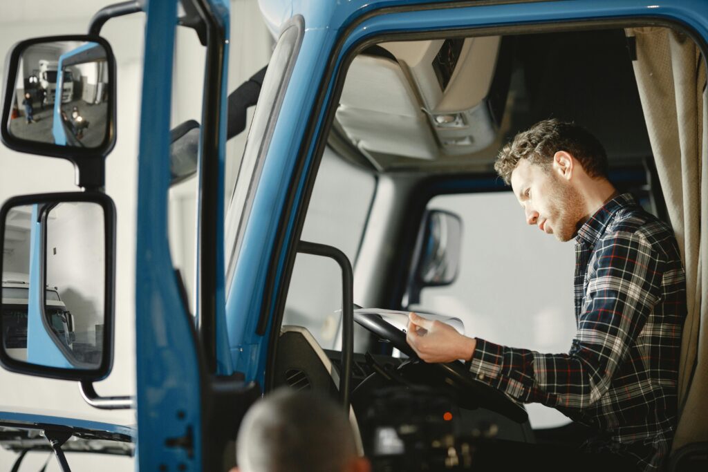 A driver looking at a clipboard in a semi truck front seat while auditing his fleet management strategies he's using for his truck operation